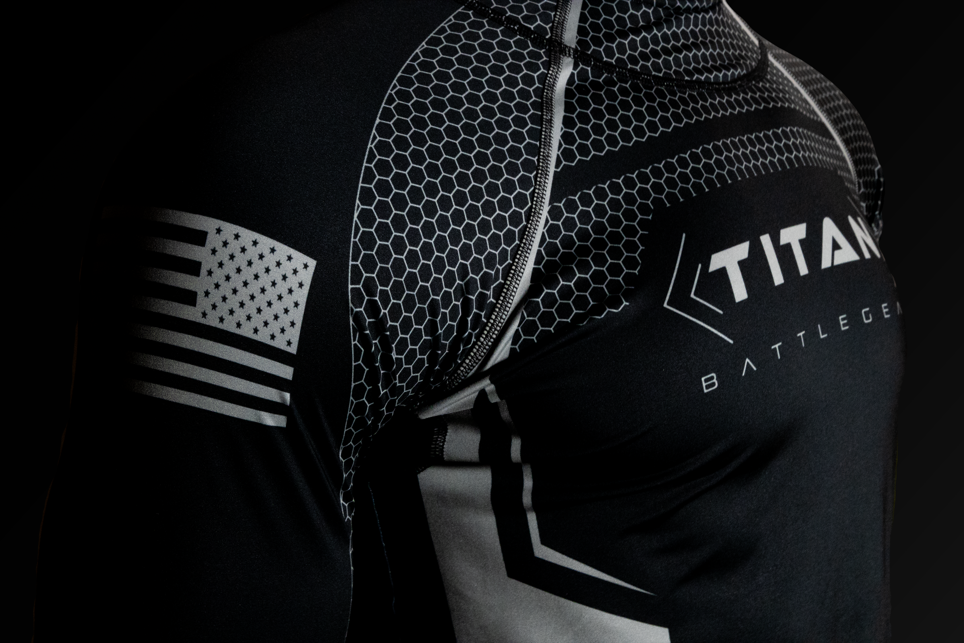 Close-up of a Titan BattleGear hockey neck guard shirt, showcasing the detailed hexagonal pattern and the Titan logo on the chest. The sleeve features an American flag design, emphasizing the shirt's craftsmanship and durability.