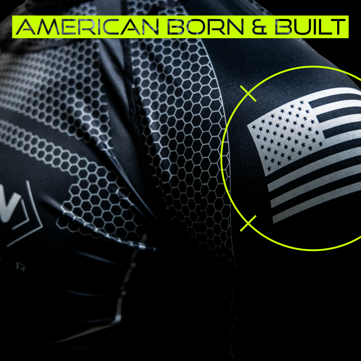 Close-up image of a Titan Battlegear shirt with an American flag emblem on the sleeve. The text "American Born & Built" is displayed at the top, highlighting the shirt's American manufacturing origin. The image emphasizes the quality and patriotic pride of the product.