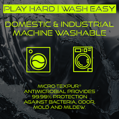 Image emphasizing the washability of Titan Battlegear. The text "Play Hard | Wash Easy" is displayed at the top, followed by "Domestic & Industrial Machine Washable." Icons of a washing machine and an industrial washer are shown, along with the note that Micro-TexPur® antimicrobial provides 99.99% protection against bacteria, odor, mold, and mildew. The background features a close-up of water splashing.